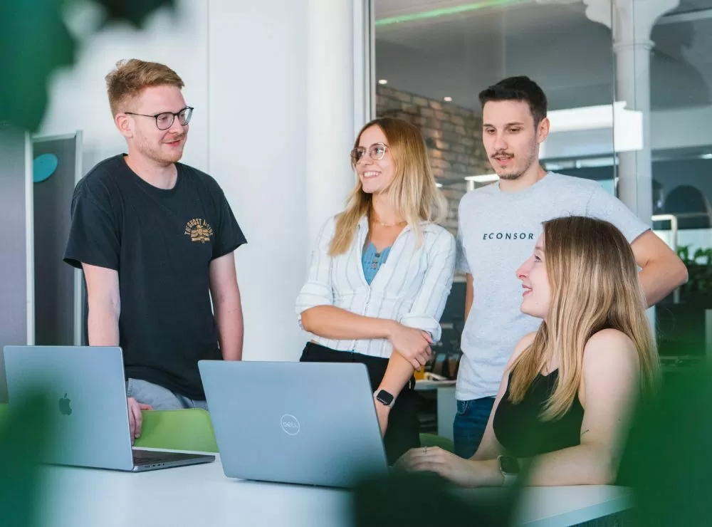 Vier Kolleginnen und Kollegen besprechen eine Online-Marketing-Konzeption an Laptops in einem modernen Büro