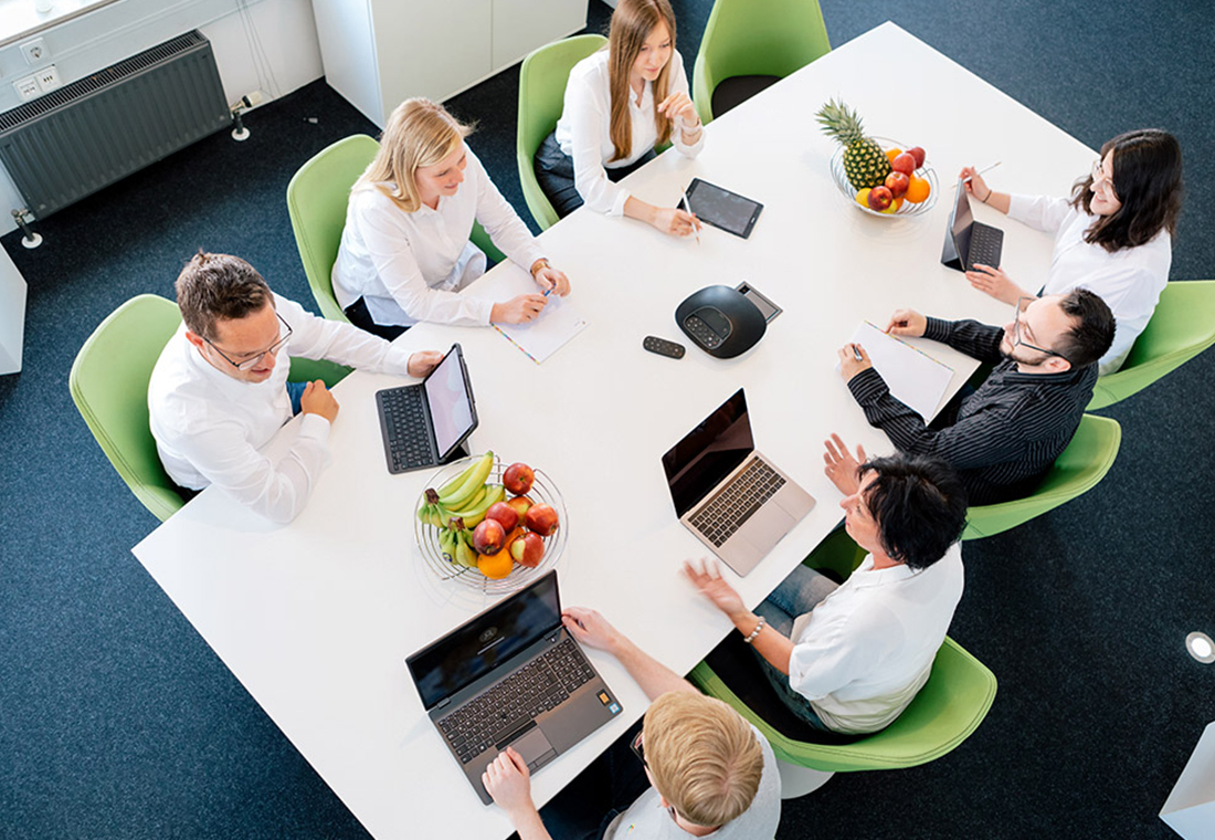Eine Gruppe von Personen sitzt um einen Tisch mit Laptops und diskutiert angeregt.
