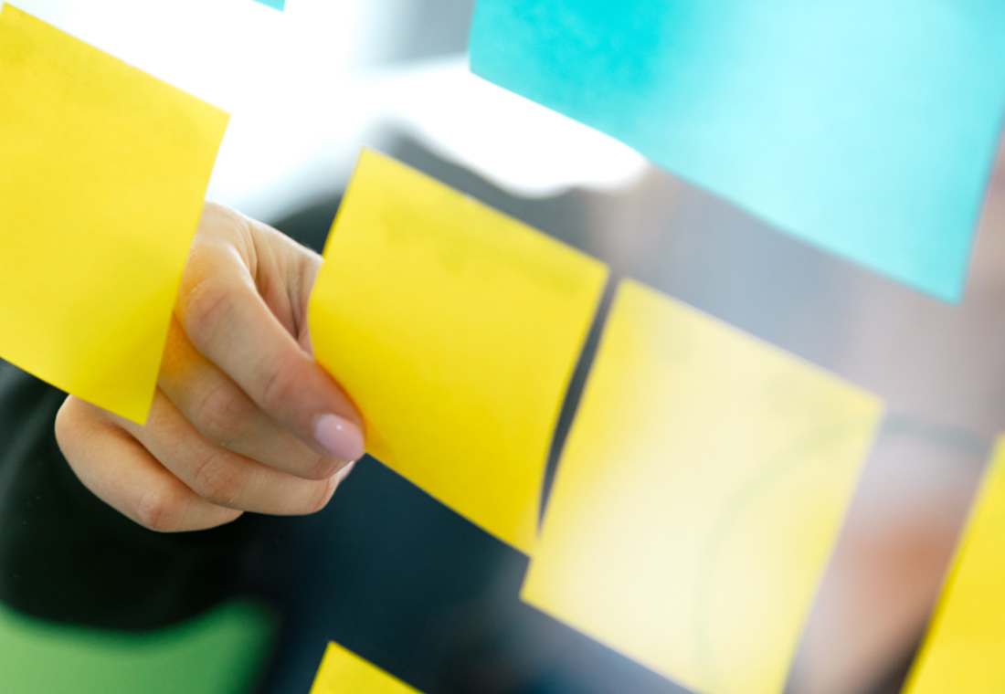 Eine Person hält ein Blatt Papier mit bunten Haftnotizen in der Hand.