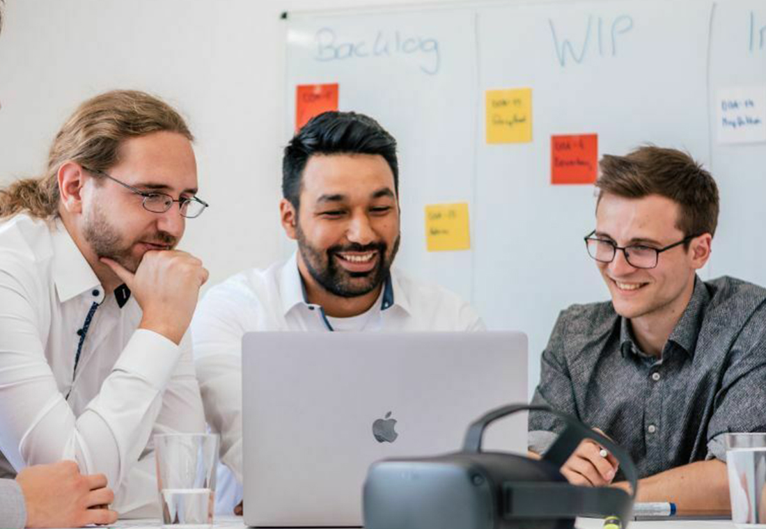 Drei Männer in einem Besprechungsraum, die um einen Laptop versammelt sind und diskutieren.
