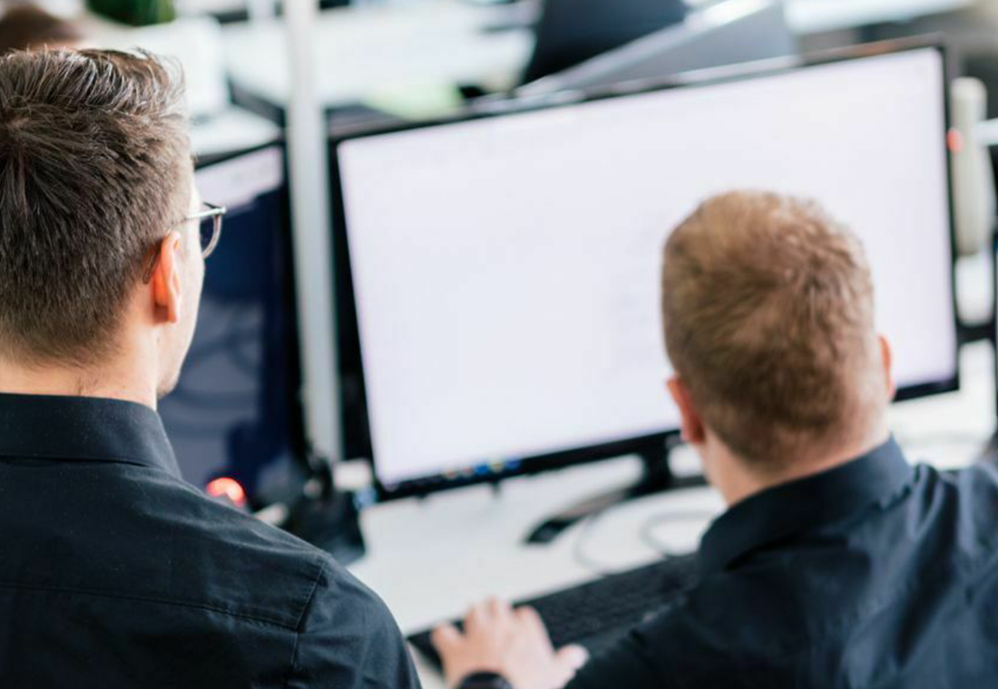 Zwei Männer in schwarzen Hemden sitzen an Computern und arbeiten konzentriert an ihren Bildschirmen.