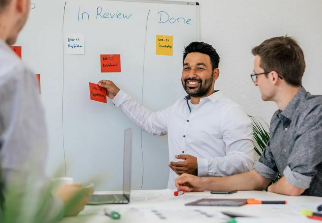 Drei Männer stehen um ein Whiteboard mit bunten Haftnotizen und diskutieren Ideen.