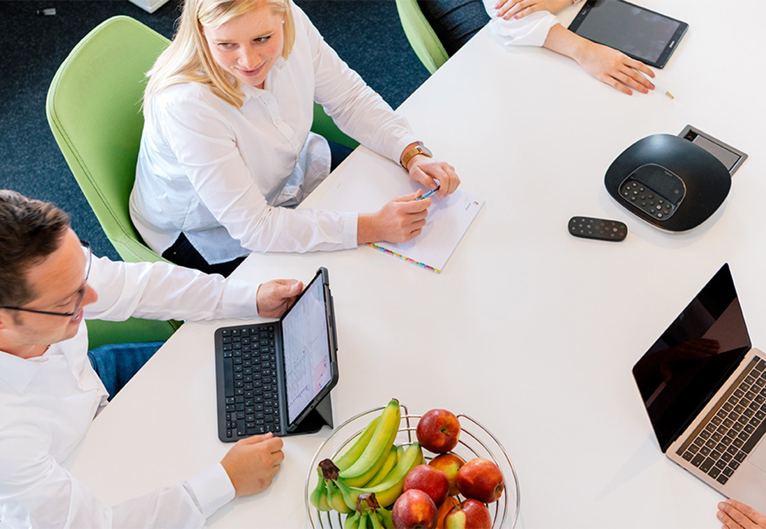 Eine Gruppe von Menschen sitzt um einen Tisch mit Laptops und diskutiert angeregt.