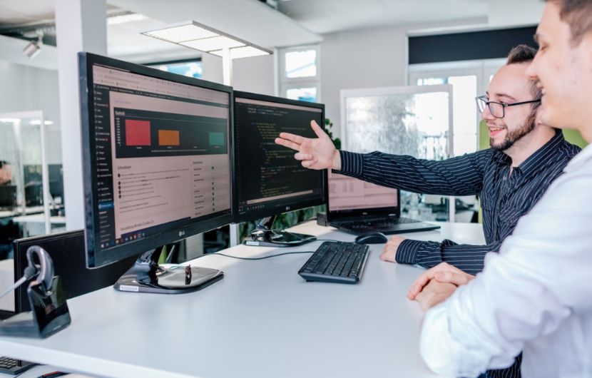 Zwei Geschäftsleute sitzen an Tisch und gemeinsam schauen in Computer Geschäftsmann zeigt mit Hand auf Bildschirm.