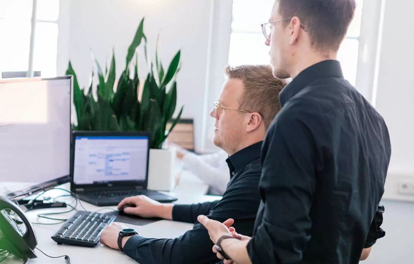 Ein Team von SEA-Experten in einem modernen Büro, umgeben von Zertifikaten und digitalen Bildschirmen, diskutiert angeregt Strategien für Google Ads Kampagnen – Symbol für eine zertifizierte Google-Ads SEA-Agentur.