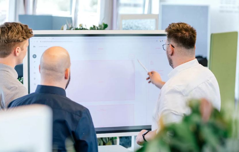 Mitarbeiter stehen vor einem digitalen Whitebaord und besprechen ein Webdesign