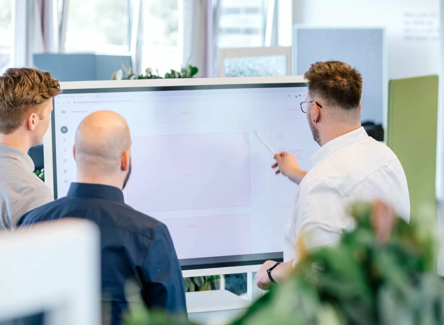 Drei Mitarbeitende arbeiten an einem Projekt auf einem großen Bildschirm