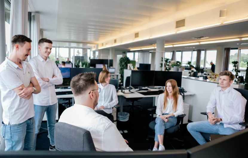 Ein erfahrener SEA-Experte berät einen Kunden an einem Schreibtisch mit Laptop und Monitor, auf dem Kampagnenstatistiken zu sehen sind – repräsentiert die individuelle Beratung einer professionellen SEA-Agentur.
