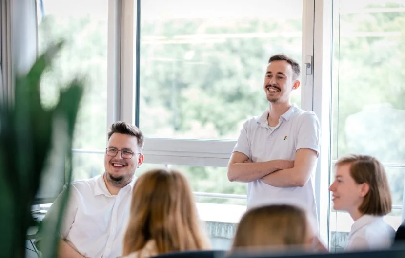 Fünf Mitarbeiter sitzen in einem Besprechungszimmer, zwei davon lächeln.