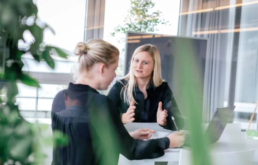 Zwei Mitarbeiterinnen befinden sich in einem Besprechungsraum mitten im Gespräch