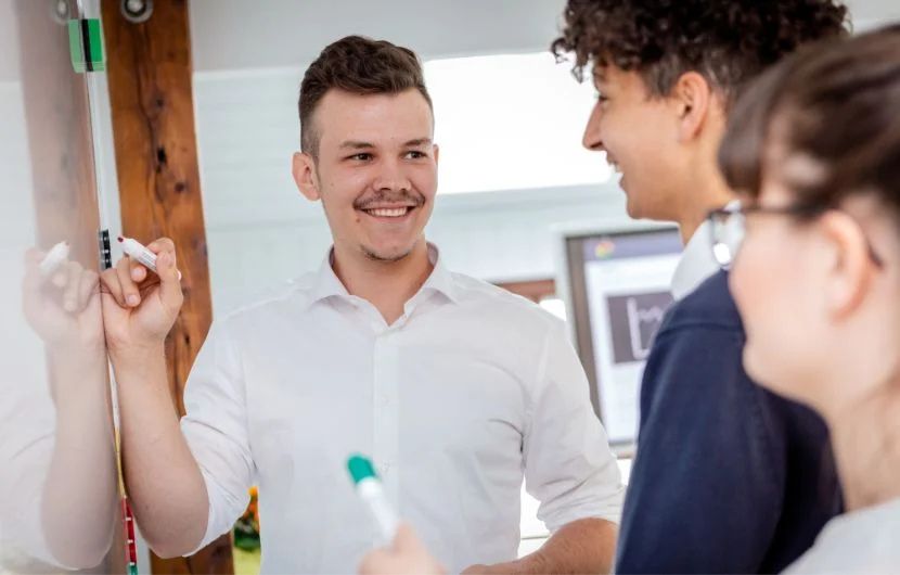 User-Research-Agentur Drei Mitarbeiter stehen an einem Whiteboard während ein Mitarbeiter etwas darauf aufzeigt