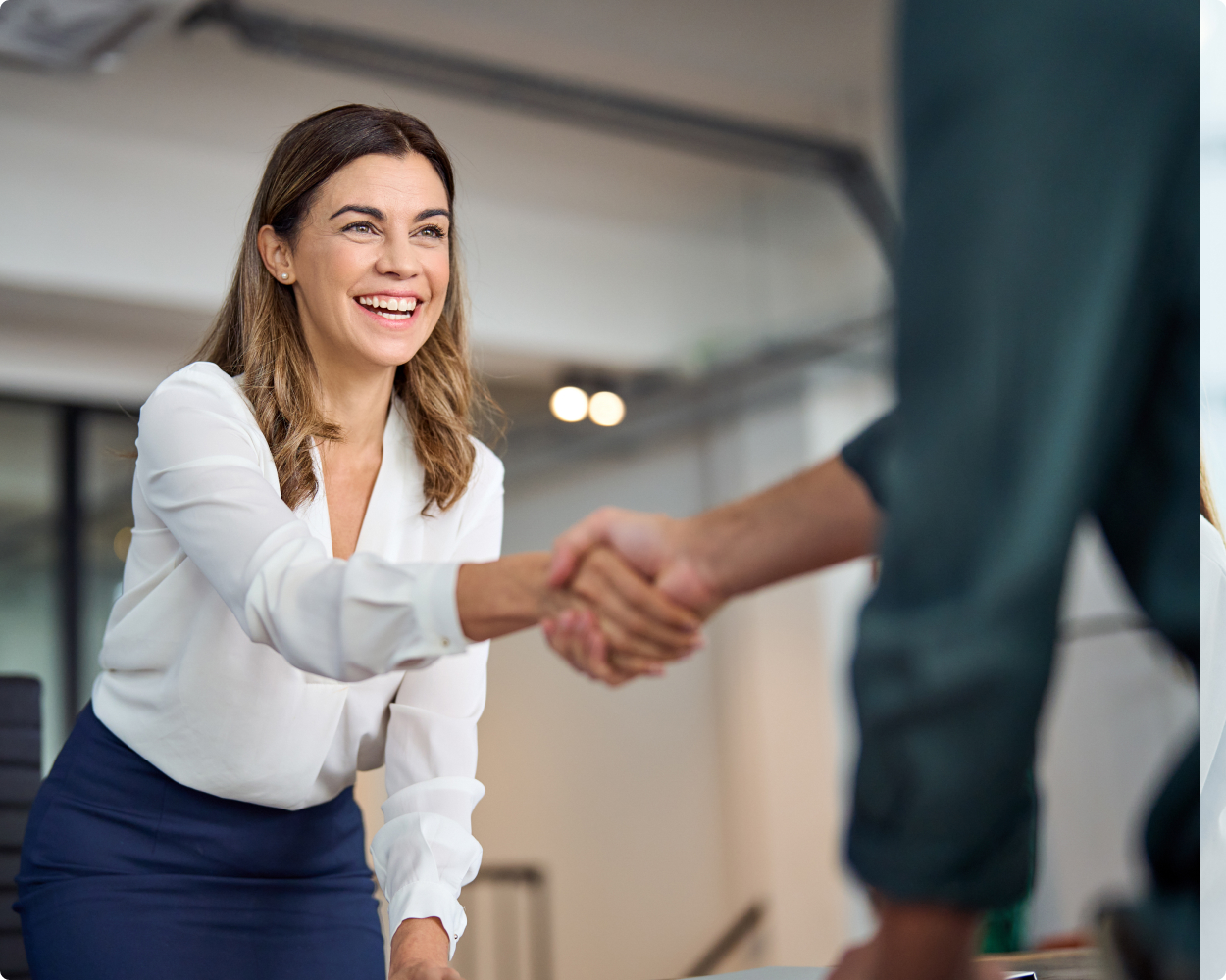 Eine Frau von VR-Networld lächelt und schüttelt einem Mann die Hand während sie aufsteht und sich über den Tisch beugt.