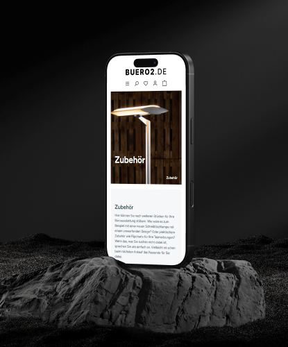 Ein Smartphone steht hochkant auf einem düsteren und unebenem Stein. Auf dem Bildschirm des Smartphones ist der Buero2-Shop abgebildet.