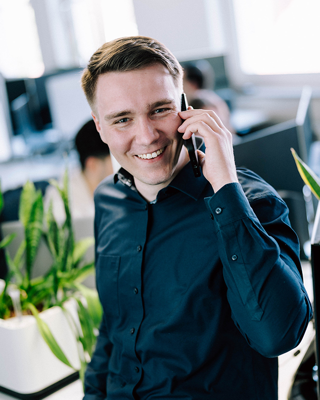 Lächelnder Agentur‑Mitarbeiter spricht am Telefon in offener Büroumgebung
