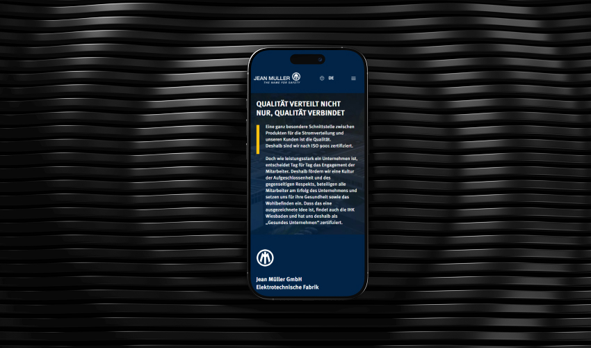 Ein Smartphone liegt flach auf einer dunklen, Oberfläche. Auf dem Bildschirm des Smartphones ist die Jean Müller-Wesbite abgebildet.