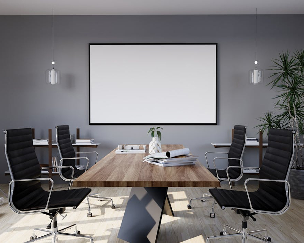 Ein im modernen und hochwertigen Stil eingerichteter Konferenzraum mir einem Holztisch und schwarzen Lederstühlen. Dahinter befindet sich eine weiße Leinwand an einer grauen Wand.
