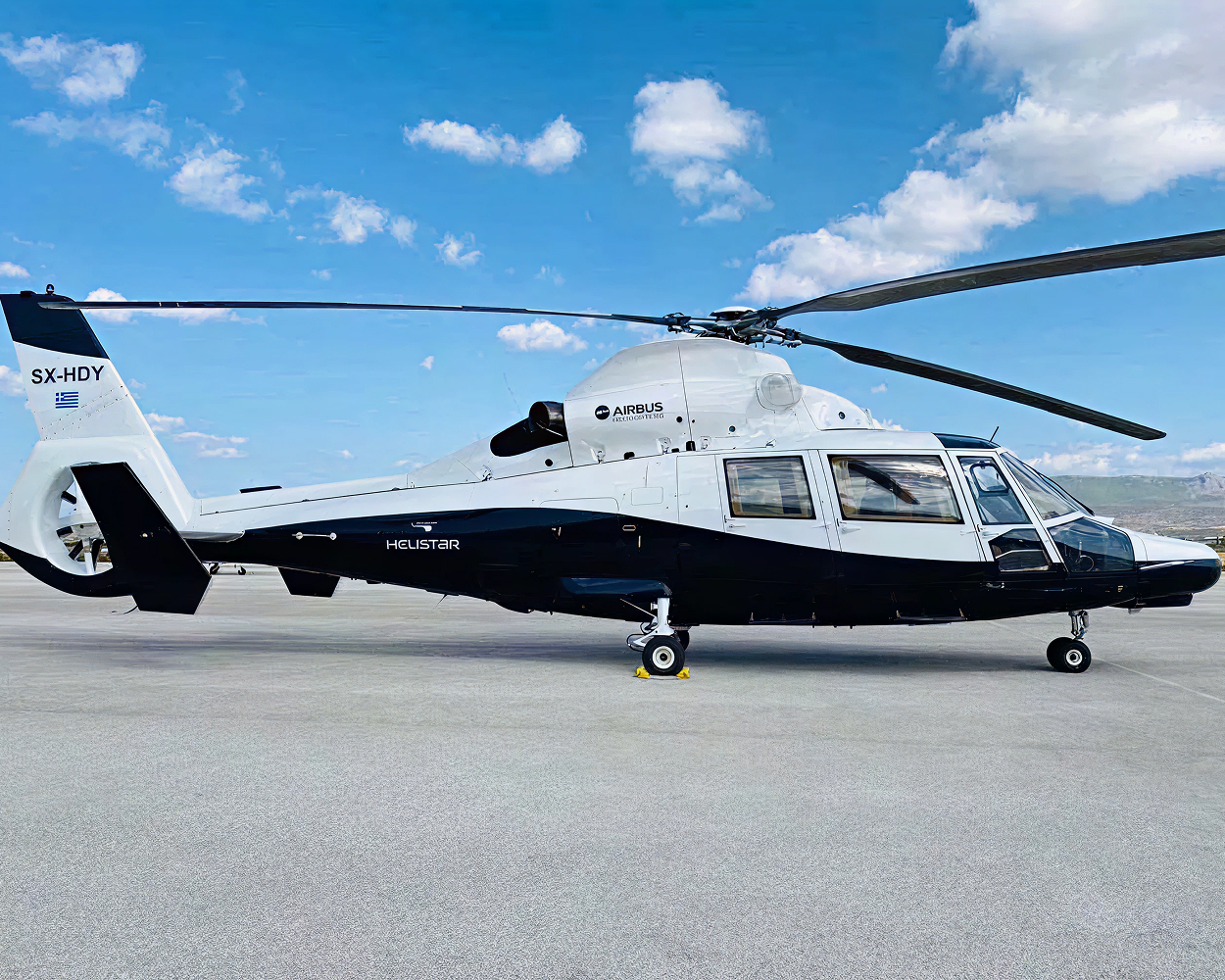 Ein Charter-Helikopter des Anbieters HELISTAR steht auf einem Flugplatz mit Betonboden. Der Himmel ist strahlend blau mit vereinzelten Wolken.
