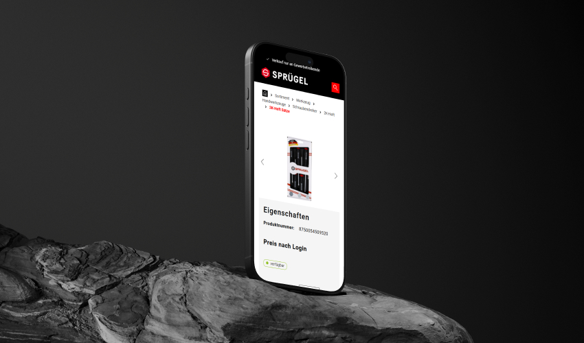 Ein Smartphone steht hochkant auf einem düsteren und unebenem Stein. Auf dem Bildschirm des Smartphones ist der Sprügel-Shop abgebildet.