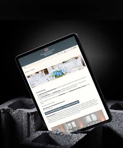 Ein Tablet steht hochkant auf einem düsteren und unebenem Stein. Auf dem Bildschirm des Tablets ist der Staatsweingut Freiburg-Shop abgebildet.