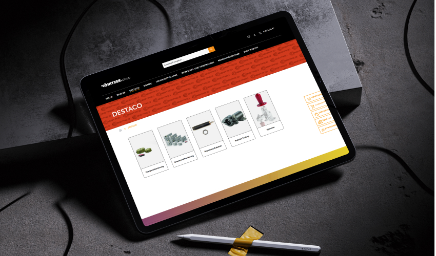Ein Tablet liegt auf einer steinigen Oberfläche. Auf dem Bildschirm des Tablets ist der KÖNITZER-Shop abgebildet.
