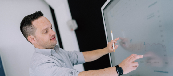 futre-to-wow Auf dem Bild ist ein Mann zu sehen, der an einem interaktiven Bildschirm arbeitet. Er zeigt mit einem Finger auf eine Grafik auf dem Bildschirm und hält dabei einen Stift in der anderen Hand