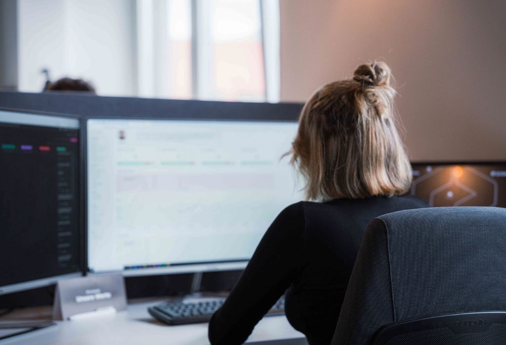 Büroarbeit in der Datenanalyse. Eine Frau arbeitet an einem Schreibtisch mit zwei Monitoren und analysiert Daten.