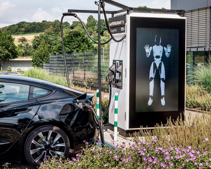 ads-tec Energy Referenz Mood Elektroauto lädt an einer Ladestation mit Roboteranzeige.