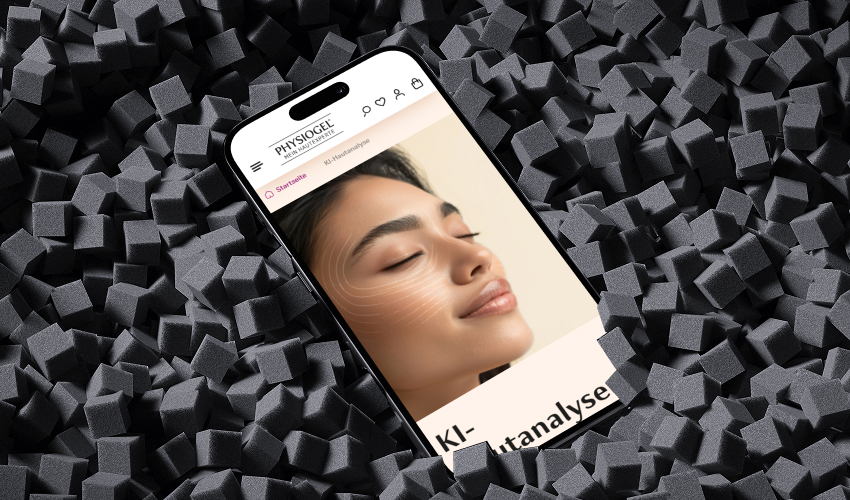 Ein Smartphone liegt flach auf einer dunklen, Schaumstoff Oberfläche. Auf dem Bildschirm des Smartphones ist der PHYSIOGEL-Shop abgebildet.
