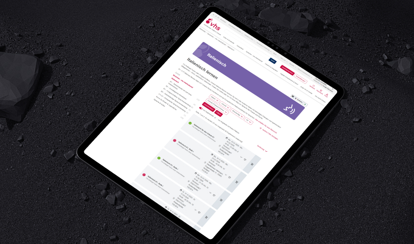 Ein Tablet liegt auf einer düsteren Oberfläche. Auf dem Bildschirm des Tablets ist die vhs-Website abgebildet.