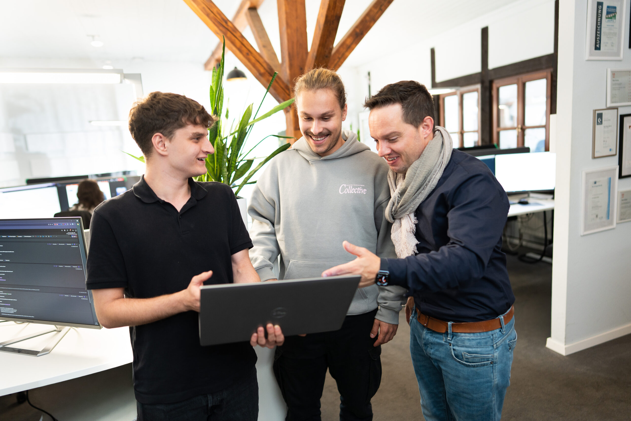 Shopware_Branchen_Fokus Drei Männer stehen in einem modernen Büro zusammen und schauen gemeinsam auf einen Laptop, während einer etwas auf dem Bildschirm erklärt.