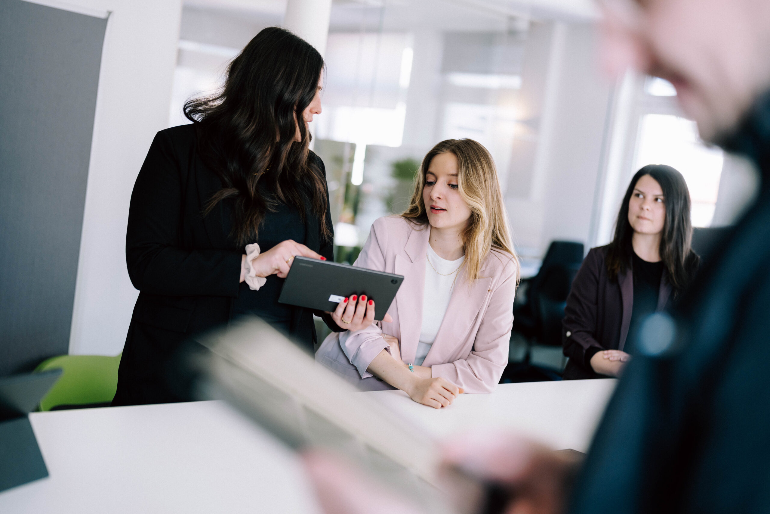 2025-04-11_c-marcel-ditrich_econsor-hn_066 Zwei Frauen betrachten gemeinsam ein Tablet, eine weitere sitzt im Hintergrund.