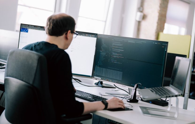 Magento_umstztung Softwareentwickler arbeitet im Büro an mehreren Monitoren mit Code und Programmierschnittstellen – konzentriertes Programmieren an einem modernen Arbeitsplatz