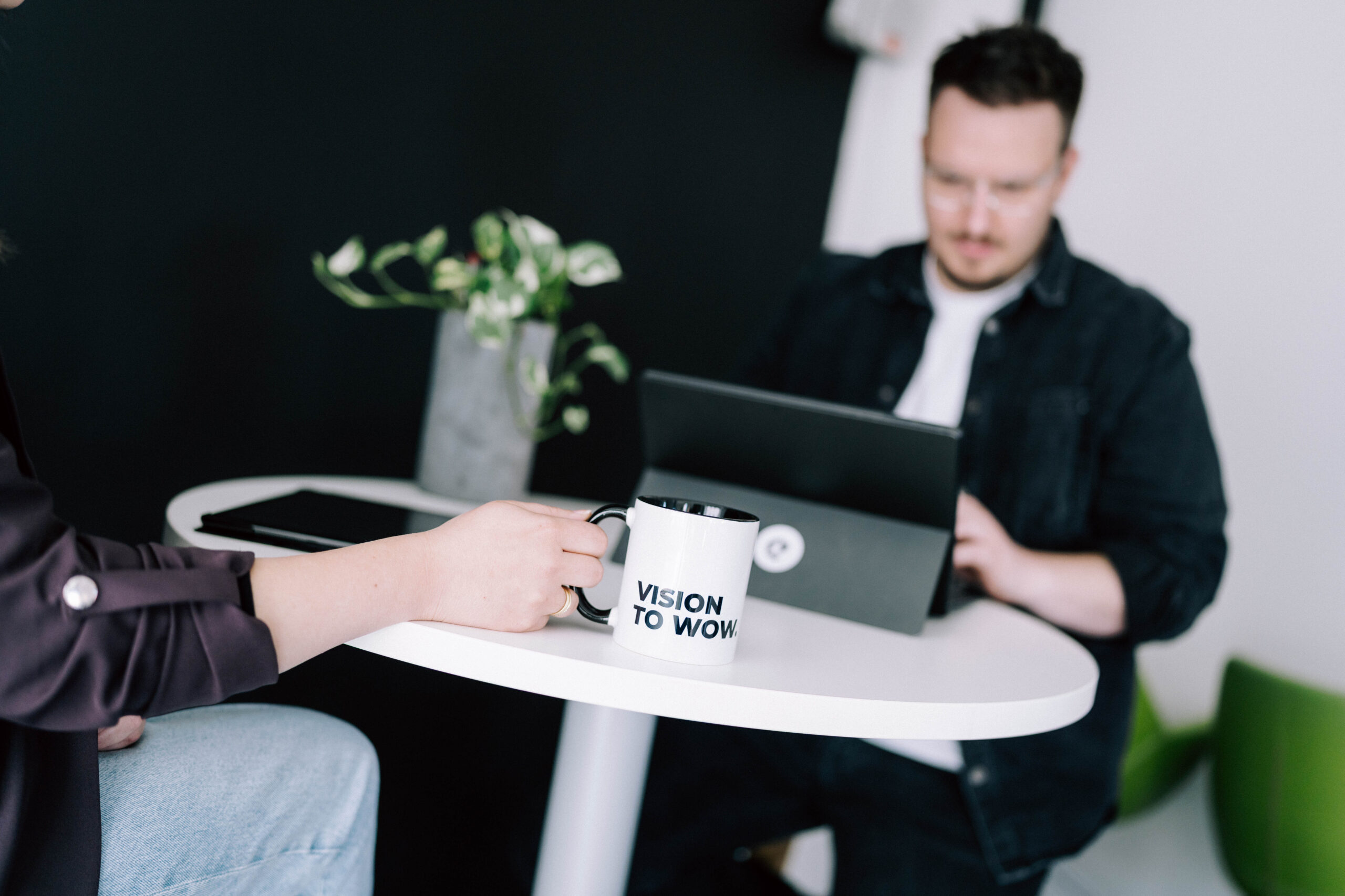 Vom Informationsangebot zum digitalen Zugangspunkt Personen im Gespräch an einem Tisch mit VISION TO WOW Tasse und Laptop.