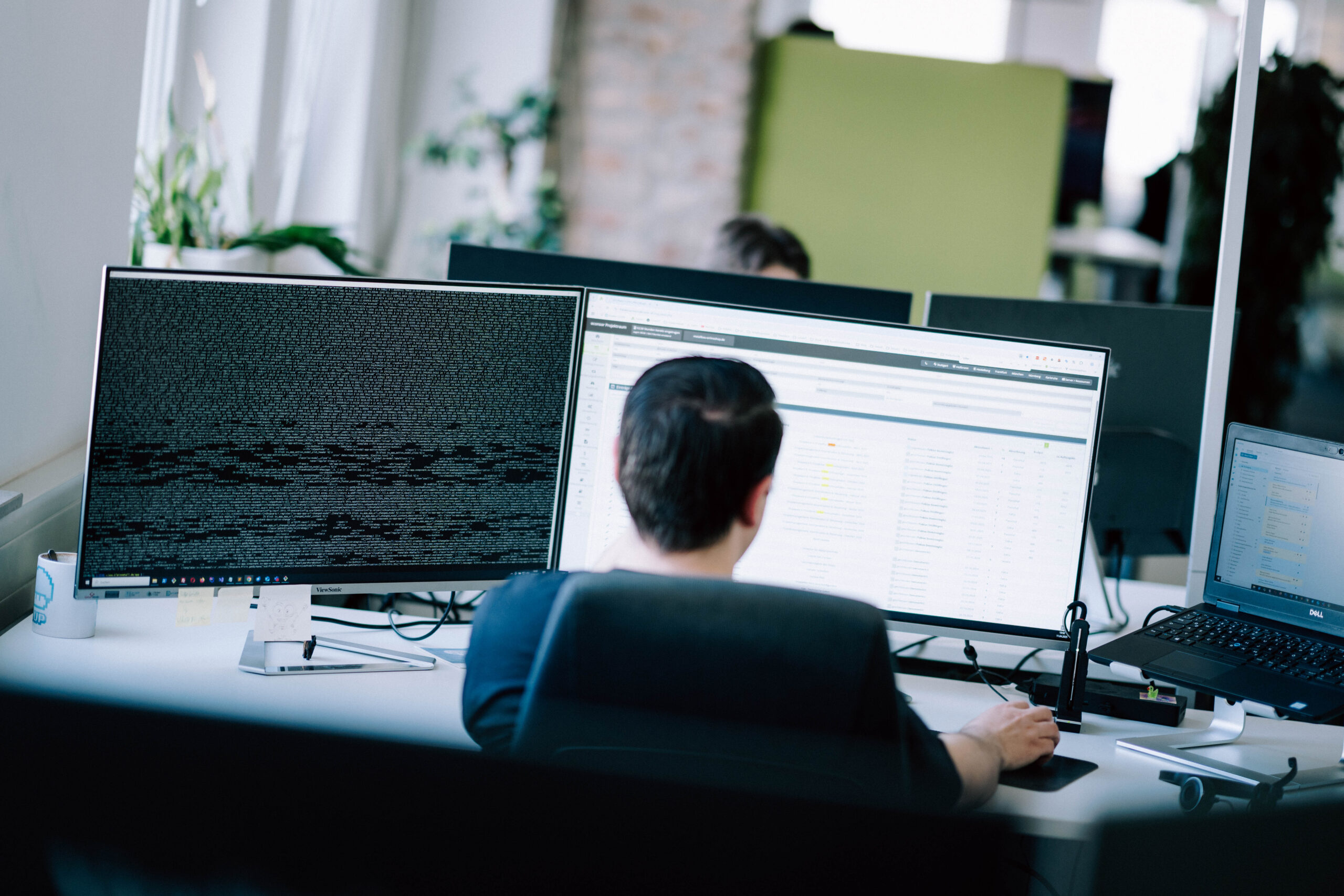 Ki schreibt eigene Software Entwickler arbeitet an mehreren Monitoren mit Code und Softwareoberfläche in einem modernen Büro.