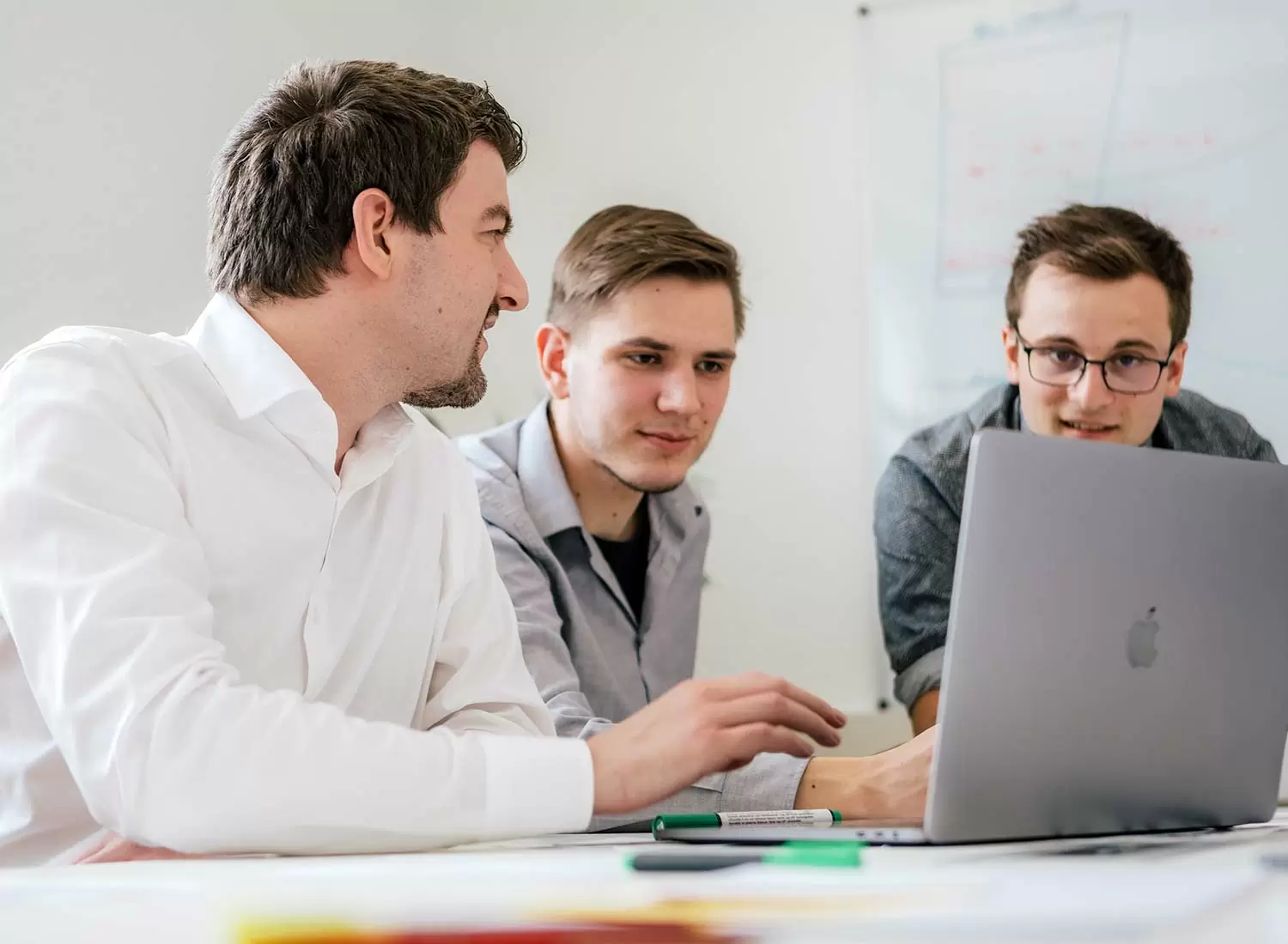 Drei Männer sitzen vor einem Computer und besprechen sich