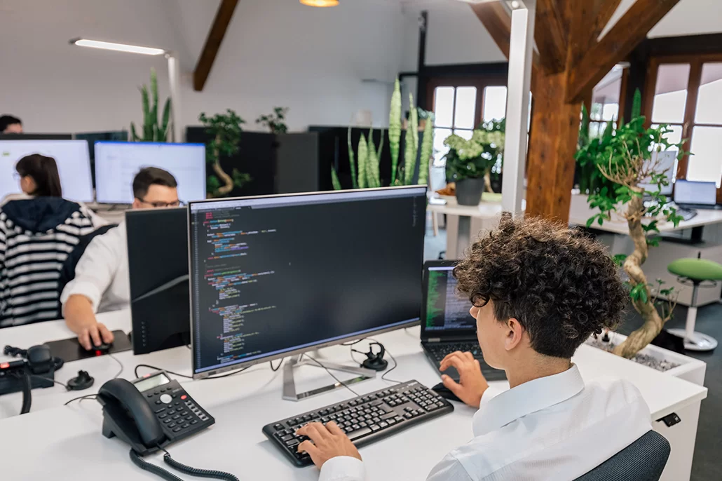 Mitarbeiter sitzt am Computer und bearbeitet Quellcode