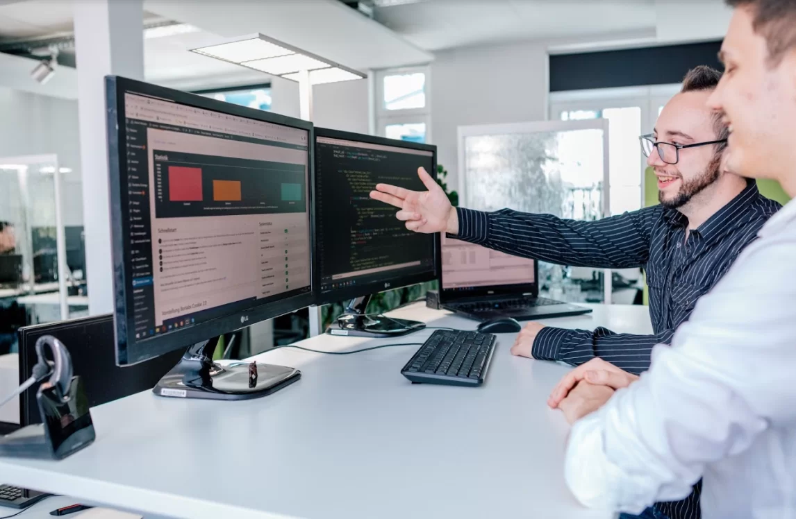 Zwei Geschäftsleute sitzen an Tisch und gemeinsam schauen in Computer Geschäftsmann zeigt mit Hand auf Bildschirm.