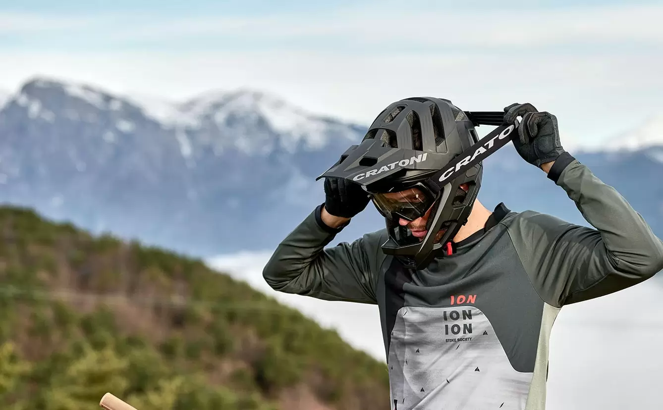 Mann zieht sich einen Cratoni Mountainbike Helm mit Brille auf