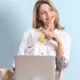 Eine Frau sitzt vor ihrem Laptop mit einer Kreditkarte in der Hand und lächelt.