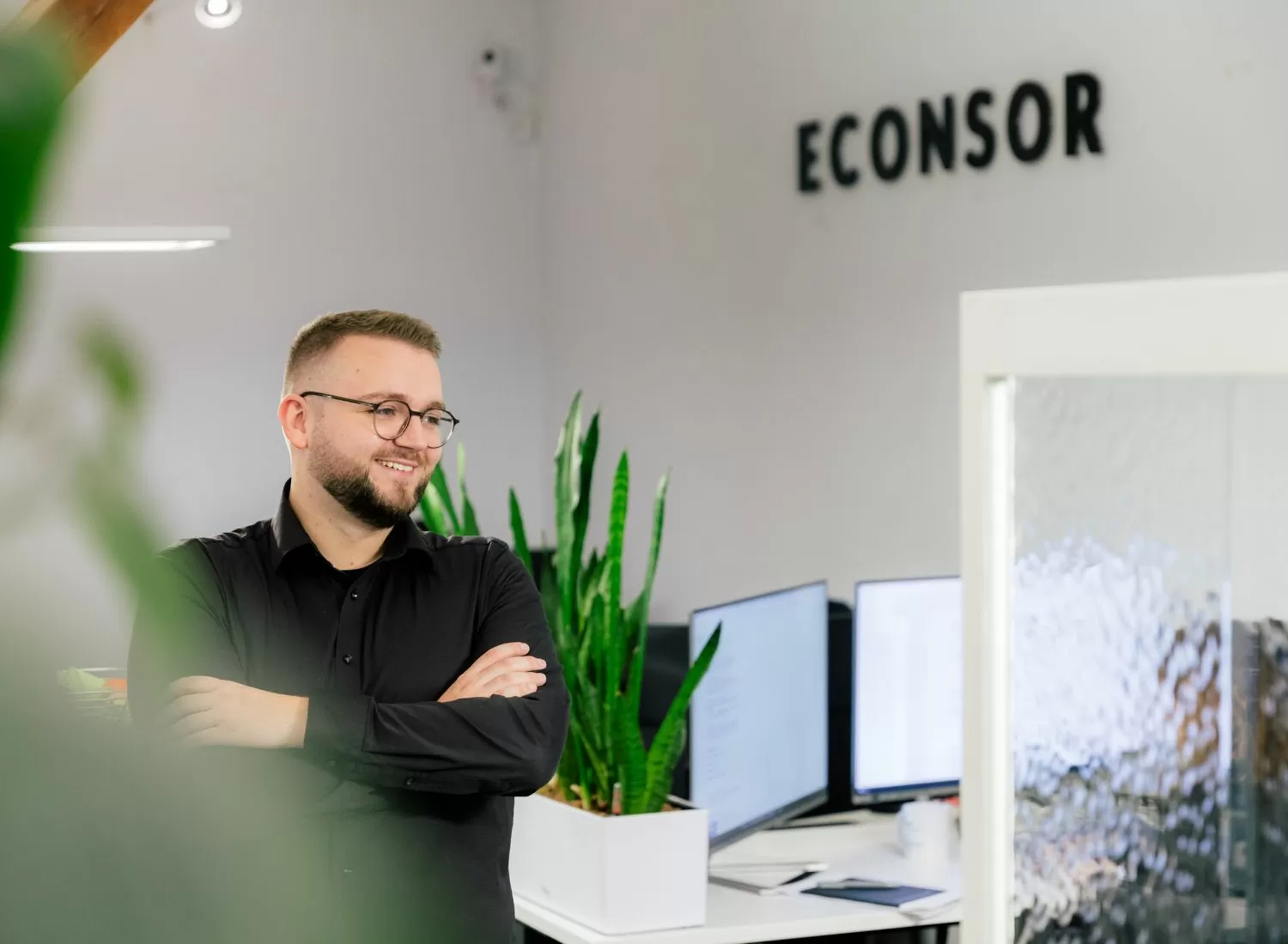 Junger mann stehe in einem Büro. Im Hintergrund sieht man Arbeitsplätze.