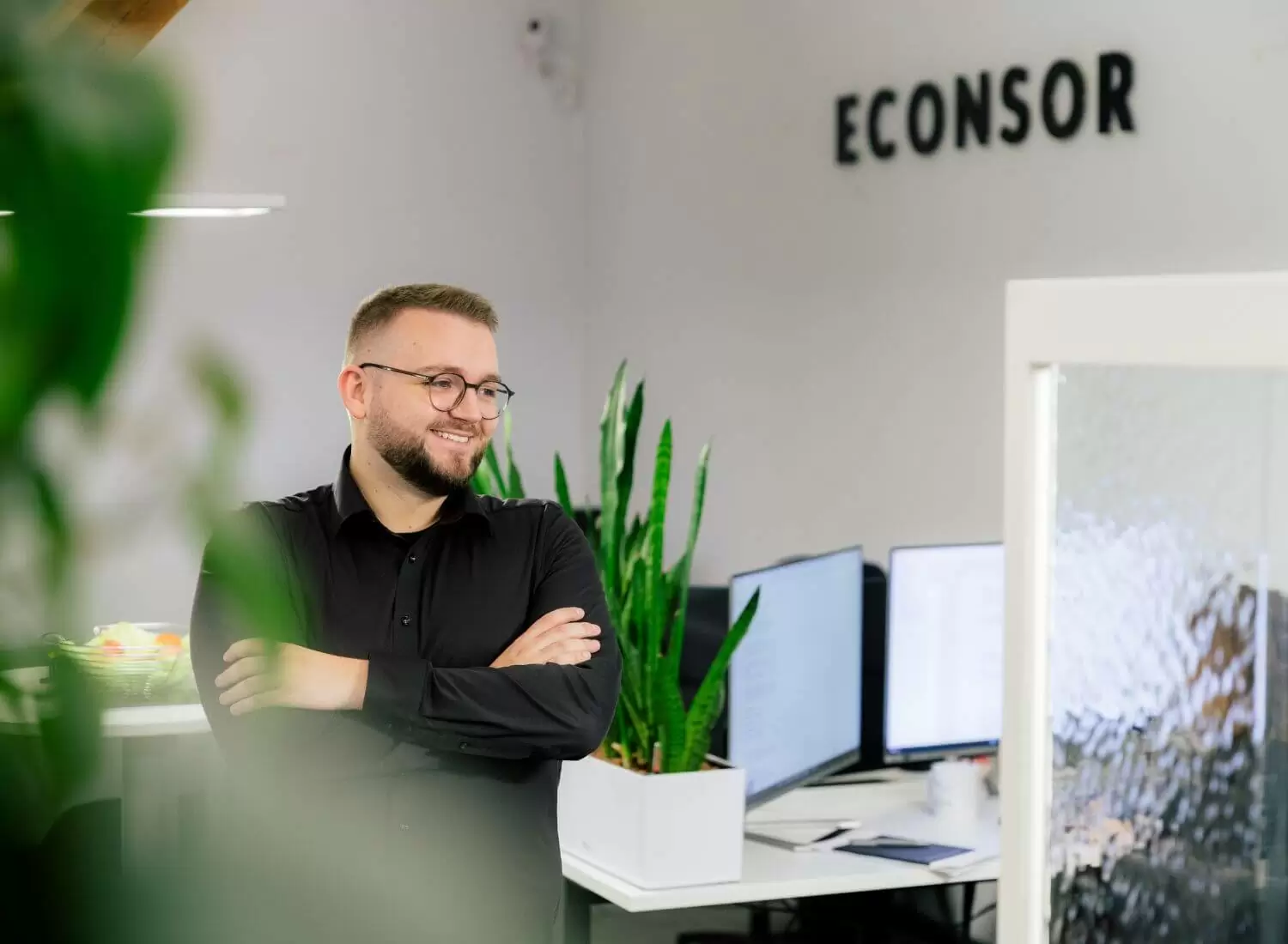 Junger mann steht in einem Büro. Im Hintergrund sieht man Arbeitsplätze.